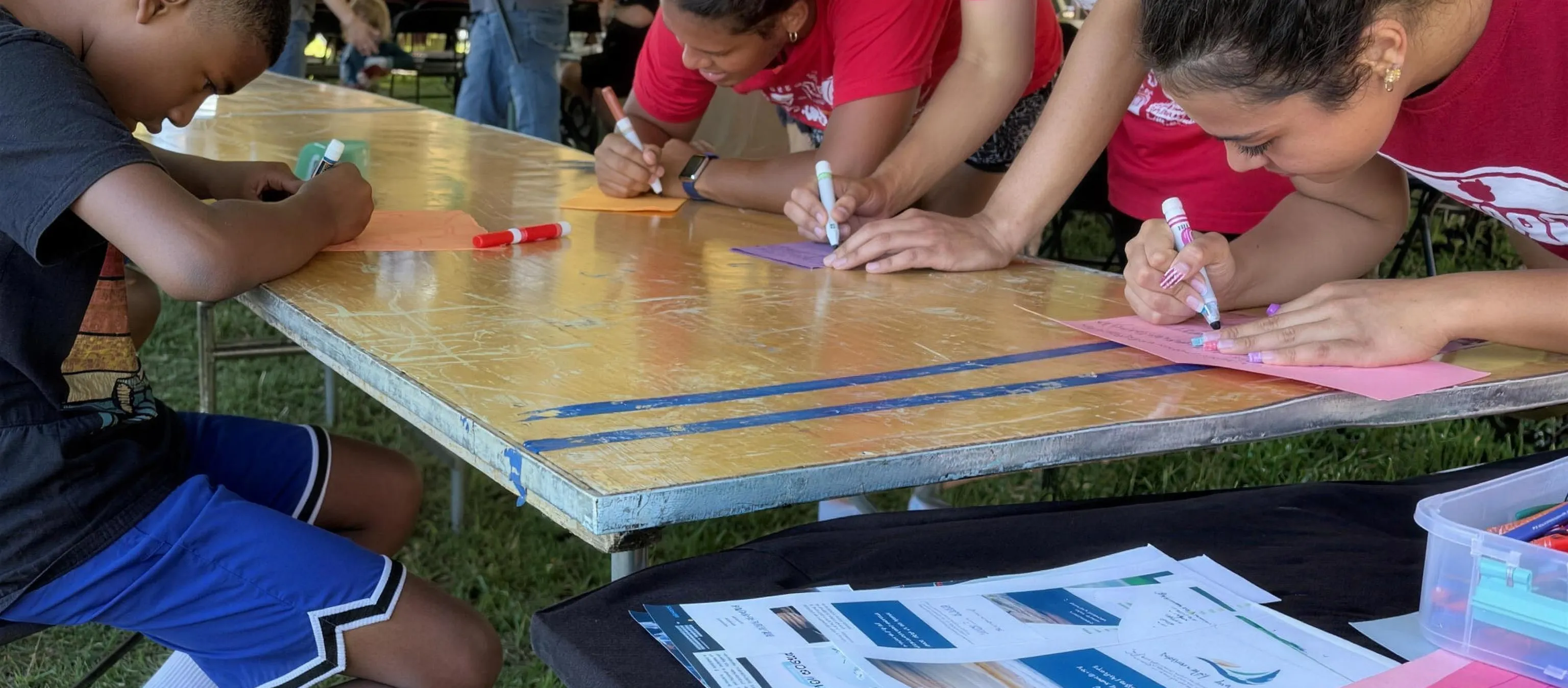 Teenagers making cards at a folding table under a tent